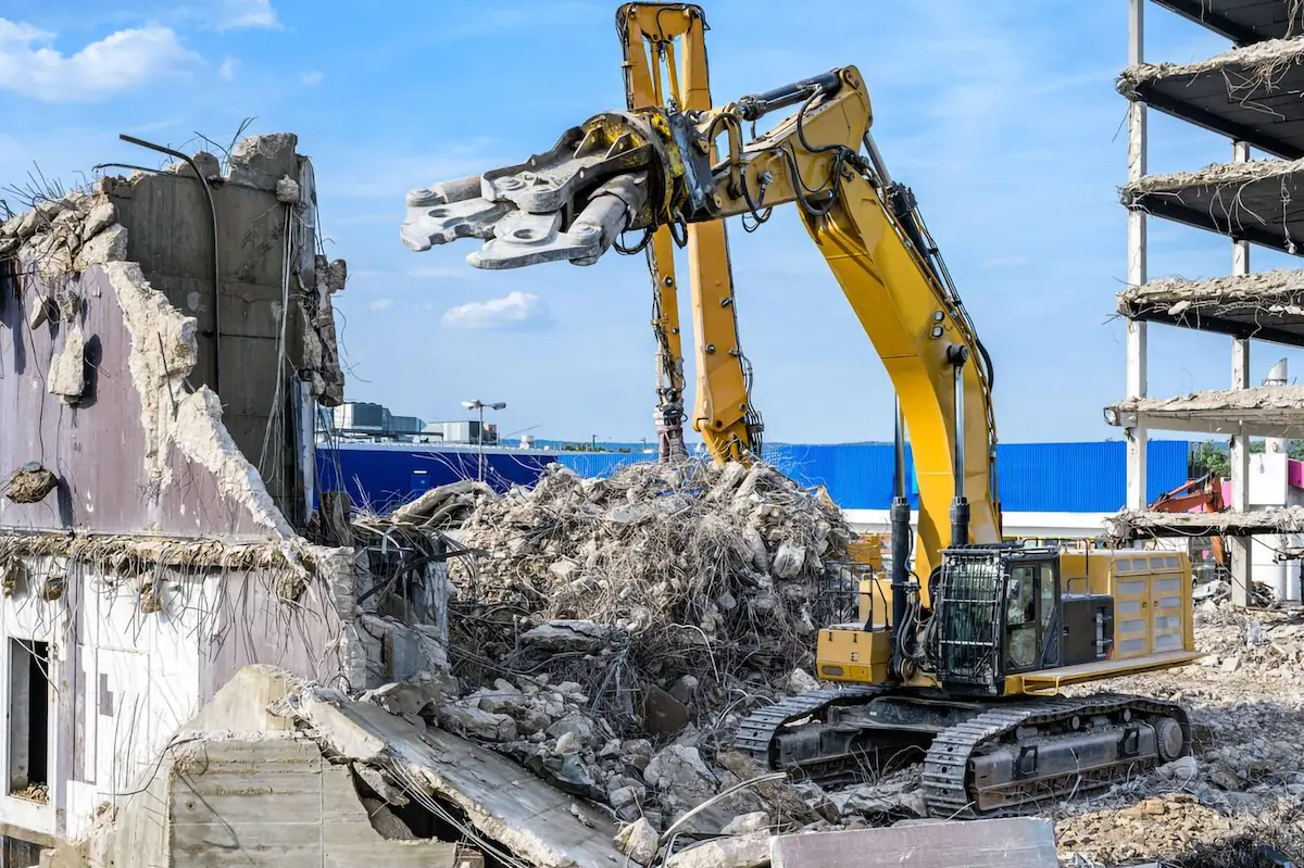 A high-reach demolition excavator equipped with Epiroc cutting scissors dismantling a reinforced concrete structure.