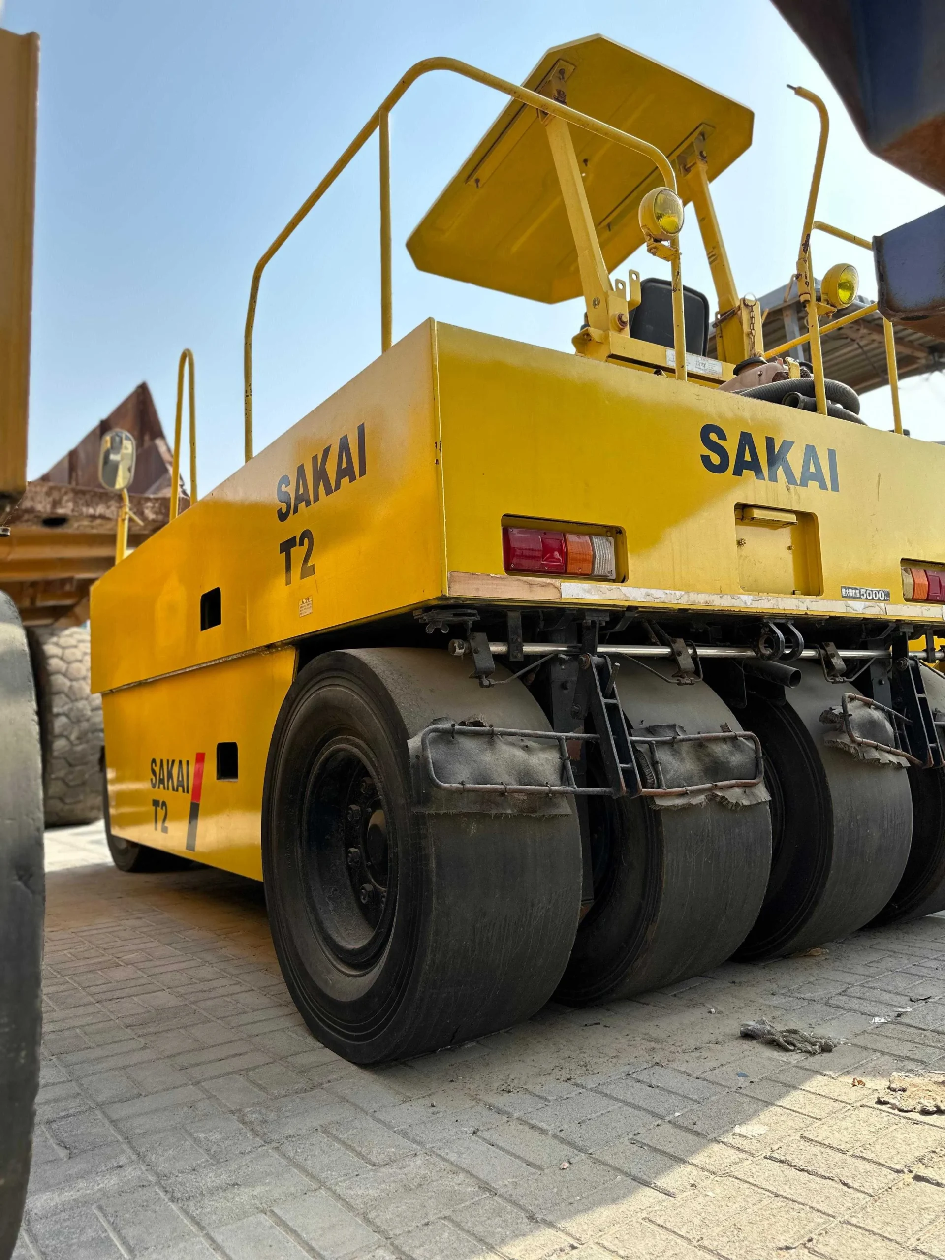 Sakai T2 asphalt roller rear three-quarter view showing the yellow body and steel drums